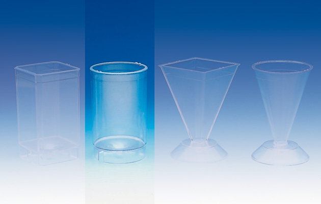 Transparente zylindrische Kerzen-Gießform (55x80 mm) mit Docht, Fixierstab und Knetmasse auf weißem Grund.